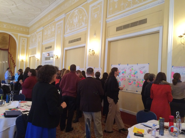 Eine Gruppe von Menschen, die Plakate und Diagramme auf einer Wand in einem scheinbar Kunstmuseum betrachten.