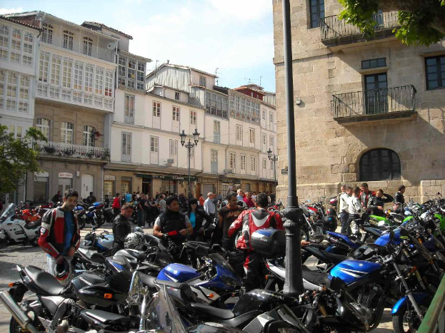 Ein cremefarbenes Gebäude mit zahlreichen Fenstern, das an ein Backsteingebäude mit einer Metallrahmen-Balkon angrenzt, mit mehreren geparkten Fahrrädern und Menschen, die vor dem Gebäude sprechen.