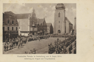 Ein Schwarz-Weiß-Foto eines Umzugs in Insterburg am 5. September 1914 mit vielen Menschen und Gebäuden im Hintergrund und einem Text am unteren Bildrand.