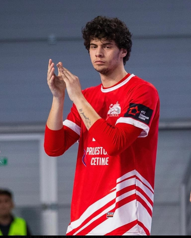 Ein Mann in einem roten und weißen Hemd, der in der Vordergrund klatscht, mit einer anderen Person und einer Wand im Hintergrund, mit dem Text "Copenhagen Futsal Club - Foto 1" unten.