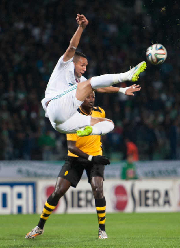 Zwei Männer beim Fußballspielen mit einem Banner im Hintergrund.