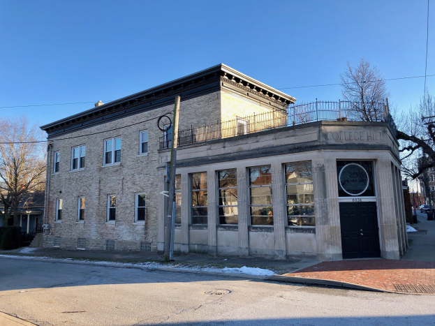 Altes Backsteingebäude mit Fenstern und einer Tür, beschriftet mit "College Hill Bibliothek", an einer Straßenecke mit Bäumen, Strommasten, Drähten, geparkten Autos und sichtbarem Himmel.
