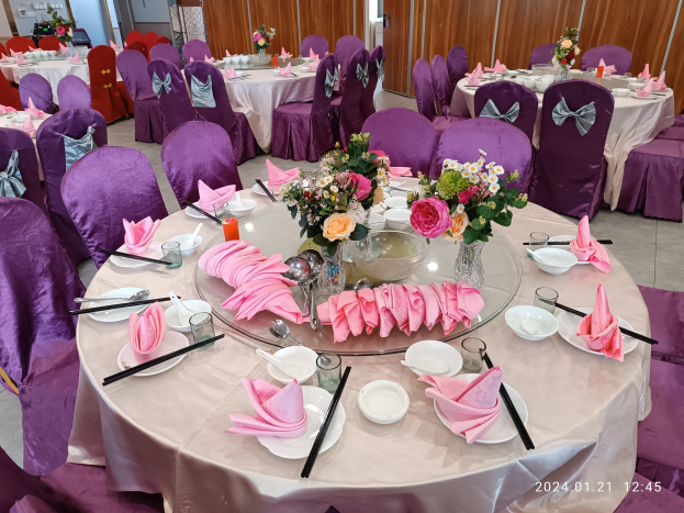 Ein Bankettsaal mit für ein formelles Ereignis gedeckten Tischen, mit Tellern, Besteck, Servietten, Blumenvasen und anderem Tafelgeschirr im Hintergrund.