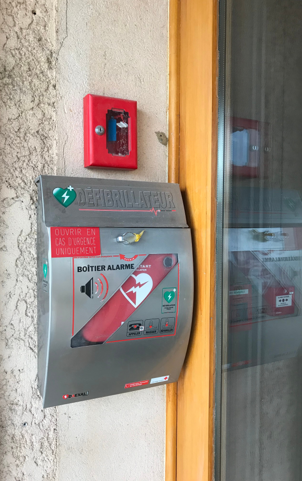 Eine rote Feueralarmanlage mit einer Glastür auf der rechten Seite, die an der Seite eines Gebäudes montiert ist, das auch ein Defibrillatorgerät ist.