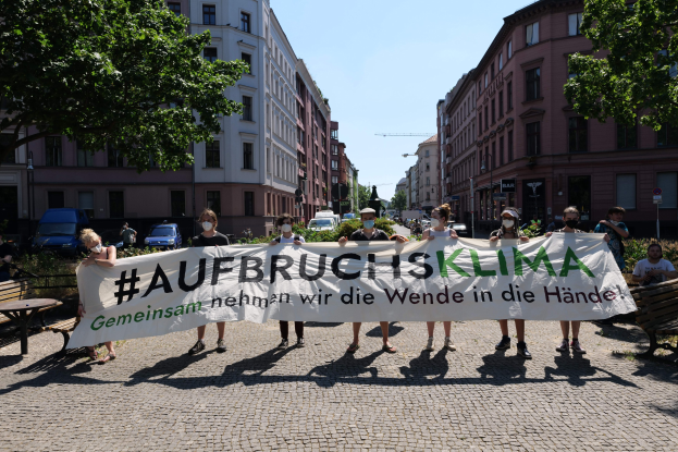 Eine Gruppe von Menschen mit Masken, die ein Transparent mit der Aufschrift 'Aufbruchsklima' tragen, während sie auf einer Klimademonstration in Berlin, Deutschland, protestieren.