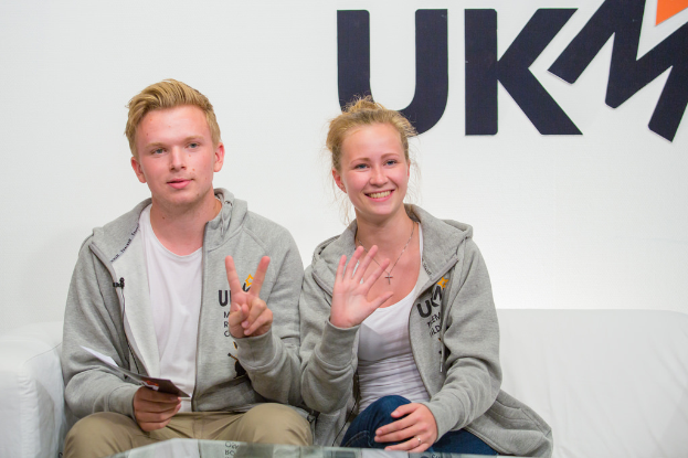 Ein Paar in passenden Jacken sitzt auf einem Sofa mit "UKM" im Hintergrund.