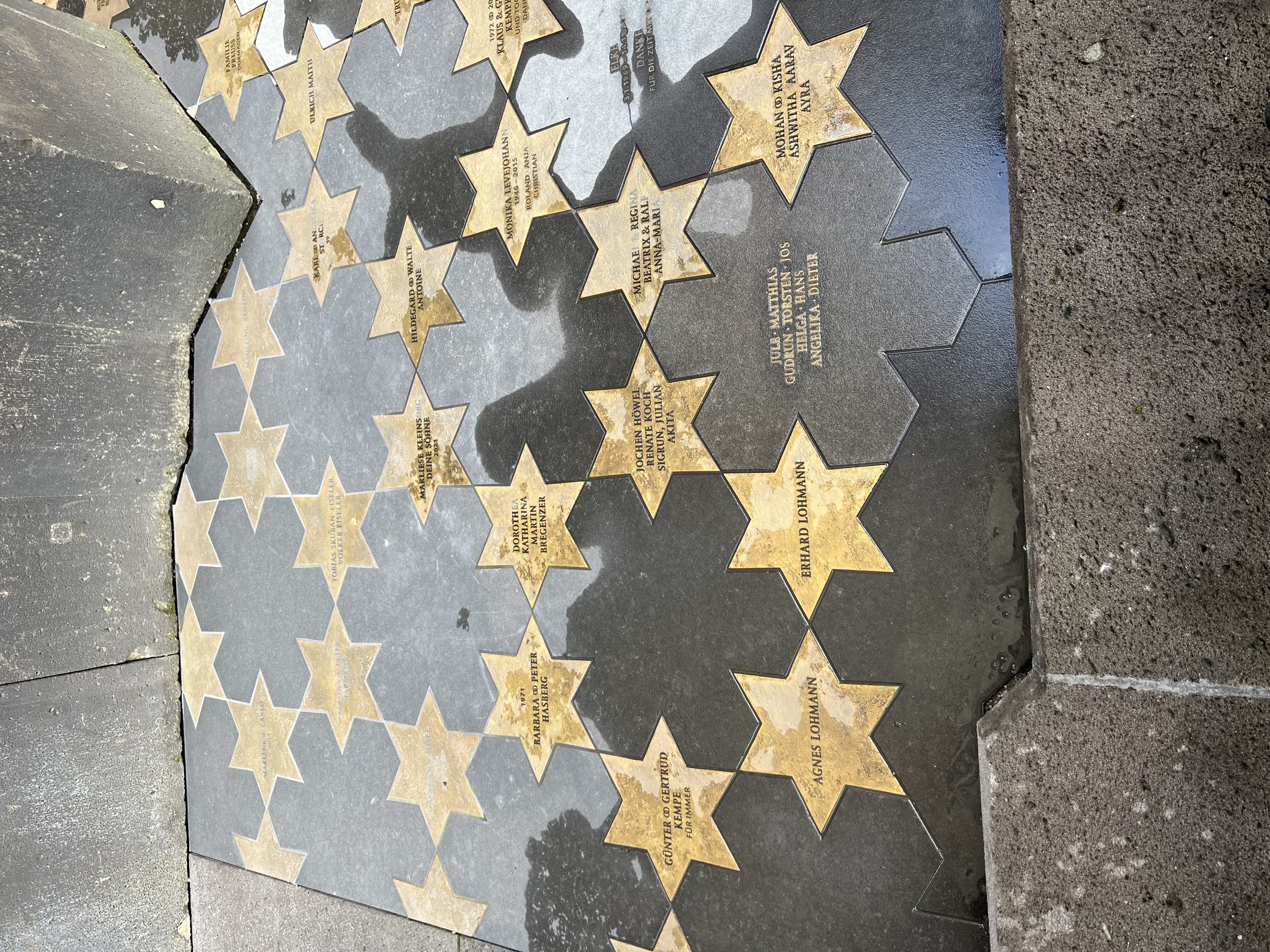 Fünf miteinander verbundene Sternplatten auf dem Hollywood Walk of Fame mit eingravierten Namen, flankiert von gefliesten Wänden.