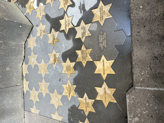 Fünf miteinander verbundene Sternplatten auf dem Hollywood Walk of Fame mit eingravierten Namen, flankiert von gefliesten Wänden.