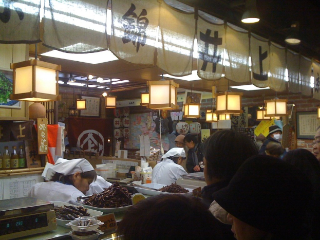 Restaurantmitarbeiter bereiten Essen hinter einer Theke mit Kunden davor, Soßenflaschen und Menükarten im Hintergrund.