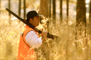Eine Person mit einer Waffe steht vor Pflanzen, mit Bäumen im Hintergrund.