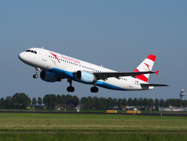 Ein Airbus A320-200 der Austrian Airlines beim Start vom Frankfurt Airport, mit grünem Gras, Bäumen, Gebäuden und einer Kontrollturm im Hintergrund.