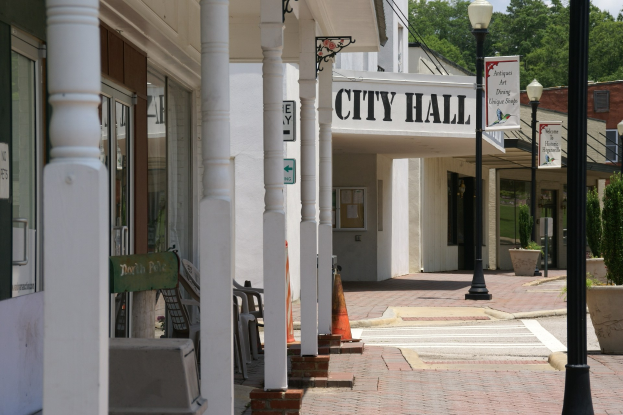 Rathaus mit umliegenden Gebäuden, Straßeninfrastruktur, Fahrzeugen, Verkehrskegeln, Möbeln, Grünflächen und einem bewölkten Himmel.