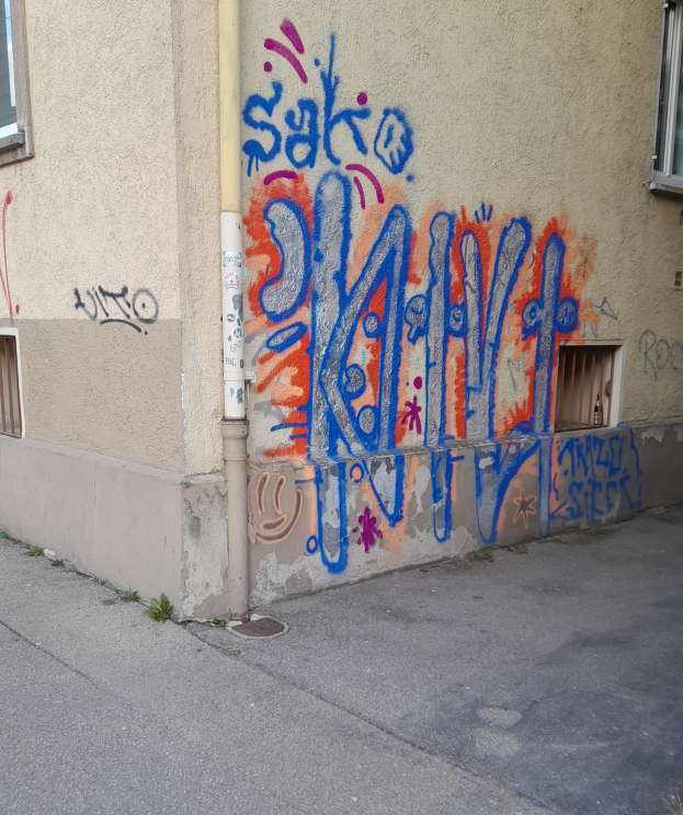 Ein Gebäude mit Fenstern, einem Rohr und Graffiti an der Seite, mit einer Straße unten im Bild.