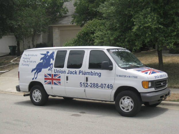 Ein Van auf der Straße mit einer Flaggengestaltung und Text auf der Seite, mit einem Haus und Bäumen im Hintergrund.