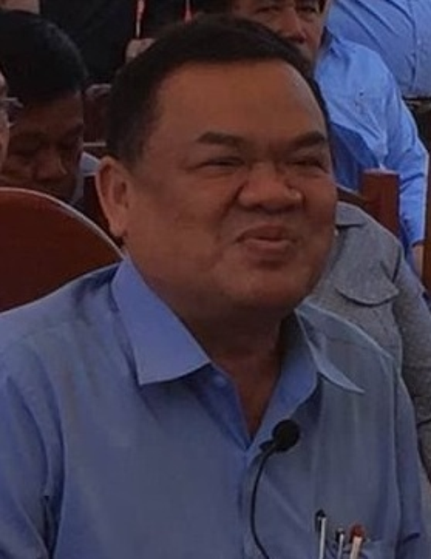 Ein Mann in einem blauen Hemd sitzt an einem Tisch mit einem Mikrofon, umgeben von einer Gruppe von Menschen, die auf Stühlen sitzen, was darauf hindeutet, dass er der CEO ist.