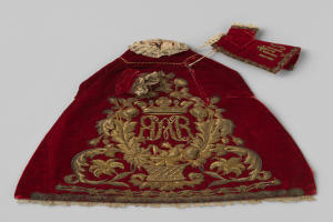 Ein roter Samtmantel mit goldener Stickerei und einer Krone, der gegen einen weißen Hintergrund gestellt ist.