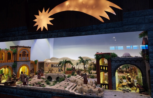 Eine Krippe-Ausstellung im Museum mit Menschen, Tieren, Häusern, Bäumen und anderen Gegenständen sowie einer beleuchteten Hintergrundgestaltung.