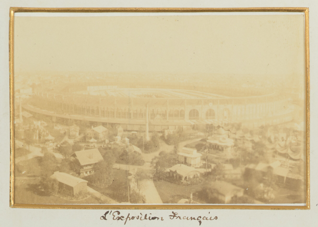 Schwarz-weiß-Foto eines Stadions in städtischer Umgebung, umgeben von Gebäuden, Bäumen und Strommasten, mit Text am unteren Rand.