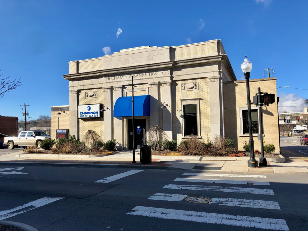 Ein Gebäude mit einem blauen Vordach an einer Straßenecke, umgeben von Pflanzen, Laternen, Fahrzeugen, Bäumen und Strommasten mit Drähten, unter einem bewölkten Himmel, identifiziert als Champion Bank & Trust Co.