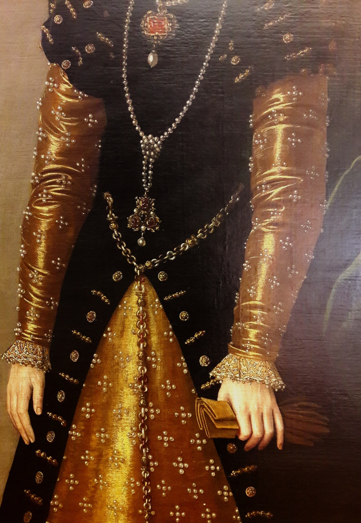 Bild einer Frau in goldenem Kleid mit hohem Ausschnitt und langen Ärmeln, die eine Tasche hält.