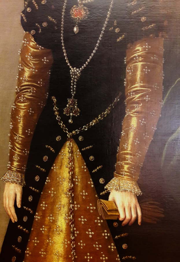 Bild einer Frau in goldenem Kleid mit hohem Ausschnitt und langen Ärmeln, die eine Tasche hält.