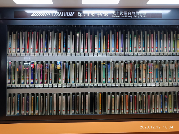 Eine gut beleuchtete Bibliothek mit hohen Bücherregalen voller Bücher, mit einem Textbrett und einem Wasserzeichen unten, das an eine Selbstbedienungsstadtbibliothek erinnert.