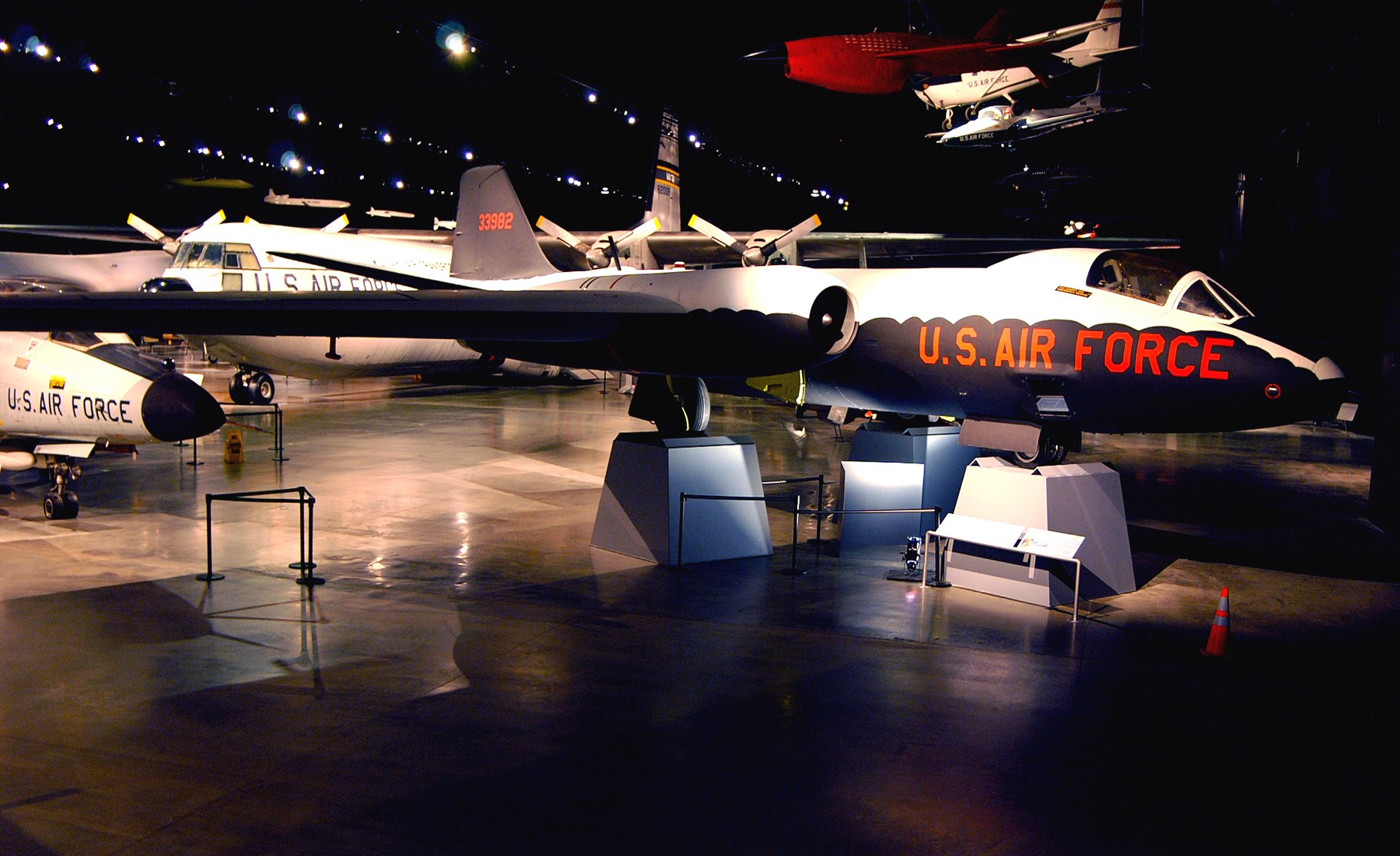 Eine Gruppe von Kampfflugzeugen in einem Museum mit St├Ąnden, Verkehrskegeln und anderen Gegenst├Ąnden auf dem Boden unter dunkler Hintergrundbeleuchtung ausgestellt.