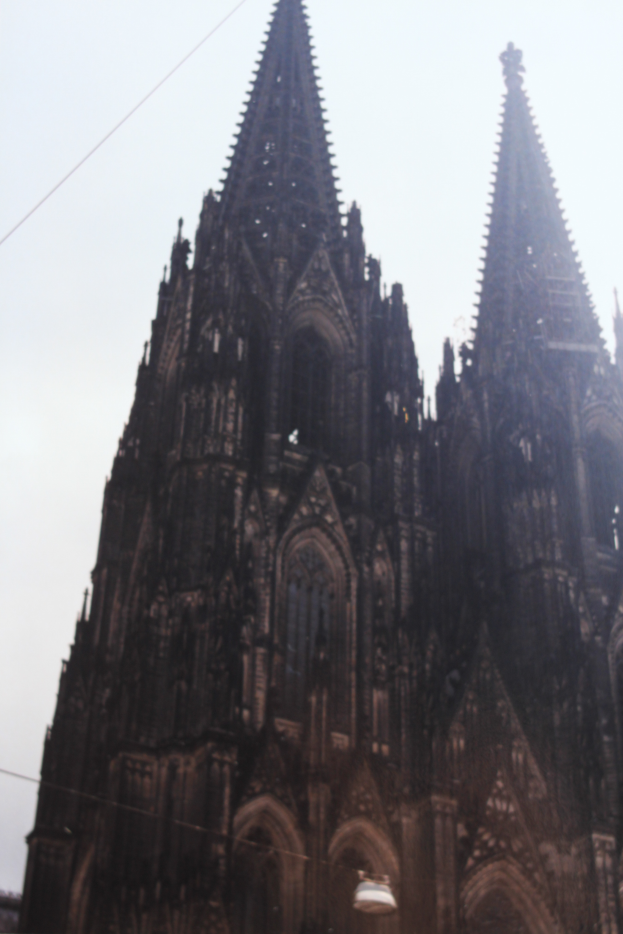 Der Kölner Dom in Köln, Deutschland, mit seinen Türmen, die in den Himmel ragen, und einigen Menschen vor dem Gebäude mit sichtbaren Kabeln im Hintergrund.