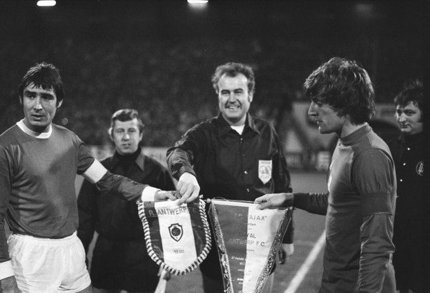 Eine Gruppe von Männern in Schwarz-Weiß-Kleidung steht zusammen auf einem Fussballfeld, zwei halten ein Schild, mit Stadionbeleuchtung oben.