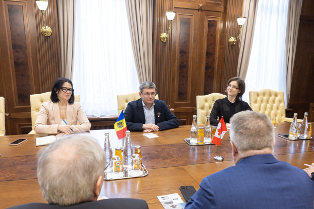 Gruppe von Menschen in einem formellen Setting um einen Holztisch mit EU-bezogenen Gegenständen, die sich in einer Diskussion befinden.