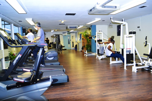 Ein Fitnessstudio mit verschiedenen Trainingsgeräten und Menschen, die trainieren, mit einer Pflanze auf der rechten Seite.