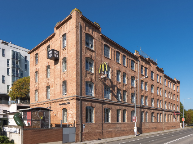 Ein großes McDonald's-Restaurantgebäude aus Backstein an einer Straßenecke in Berlin, Deutschland, mit umgebender Straßeninfrastruktur und Fahrzeugen.