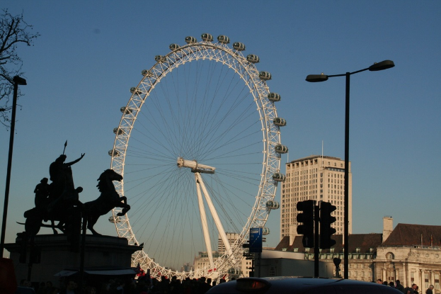 Gebäude und Masten rechts, ein große Riesenrad in der Mitte und eine Skulptur links.