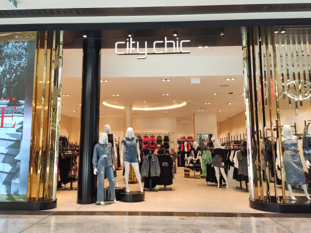 Ein stylischer Mode-Laden in einem Einkaufszentrum mit Schaufensterpuppen in der neuesten Mode, Kleidung an Bügeln, einer Säule, einem Schild, Deckenleuchten und einem gefliesten Boden.