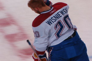 Ein Hockey-Spieler im "Wisniewski"-Trikot steht auf dem Eis und hält einen Hockey-Schläger in der Hand, mit einem konzentrierten und entschlossenen Gesichtsausdruck.
