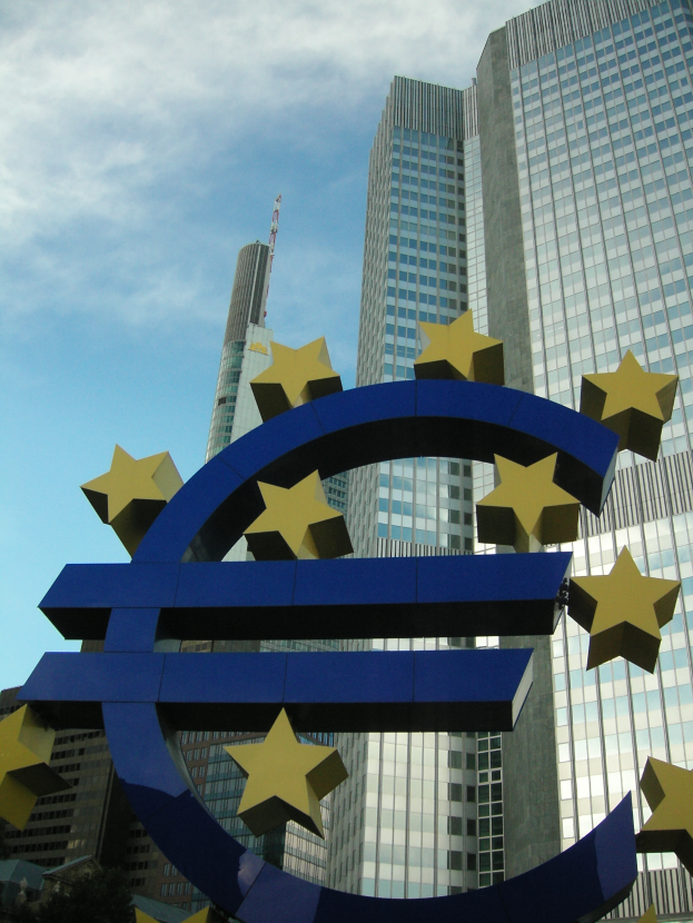 Das Euro-Zeichen steht vor dem Hauptquartier der Europäischen Zentralbank, einem großen modernen Gebäude, das von Bäumen umgeben ist und unter einem bewölkten Himmel in Frankfurt, Deutschland, steht.