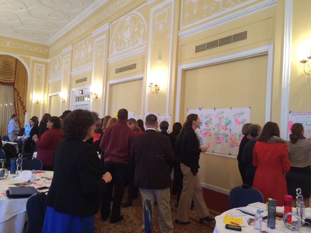 Eine Gruppe von Menschen untersucht Plakate und Diagramme, die an einer Wand in einem scheinbar künstlerischen Museum angezeigt werden.