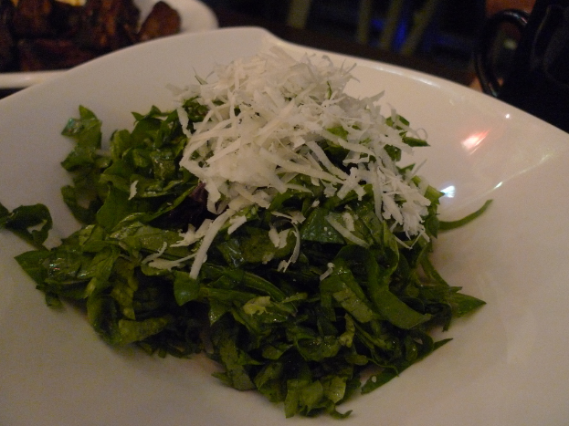 Ein Teller mit grünem Blattgemüse in der Mitte des Bildes.