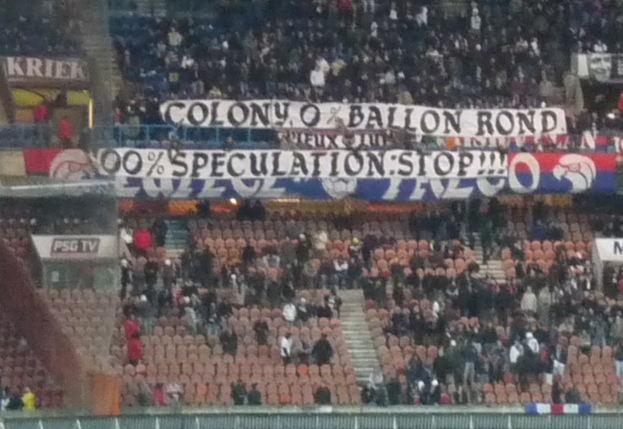 Ein Stadion voller großer Menschenmenge, Banner und Stühle, mit einem Zaun unten und einer Treppe links.
