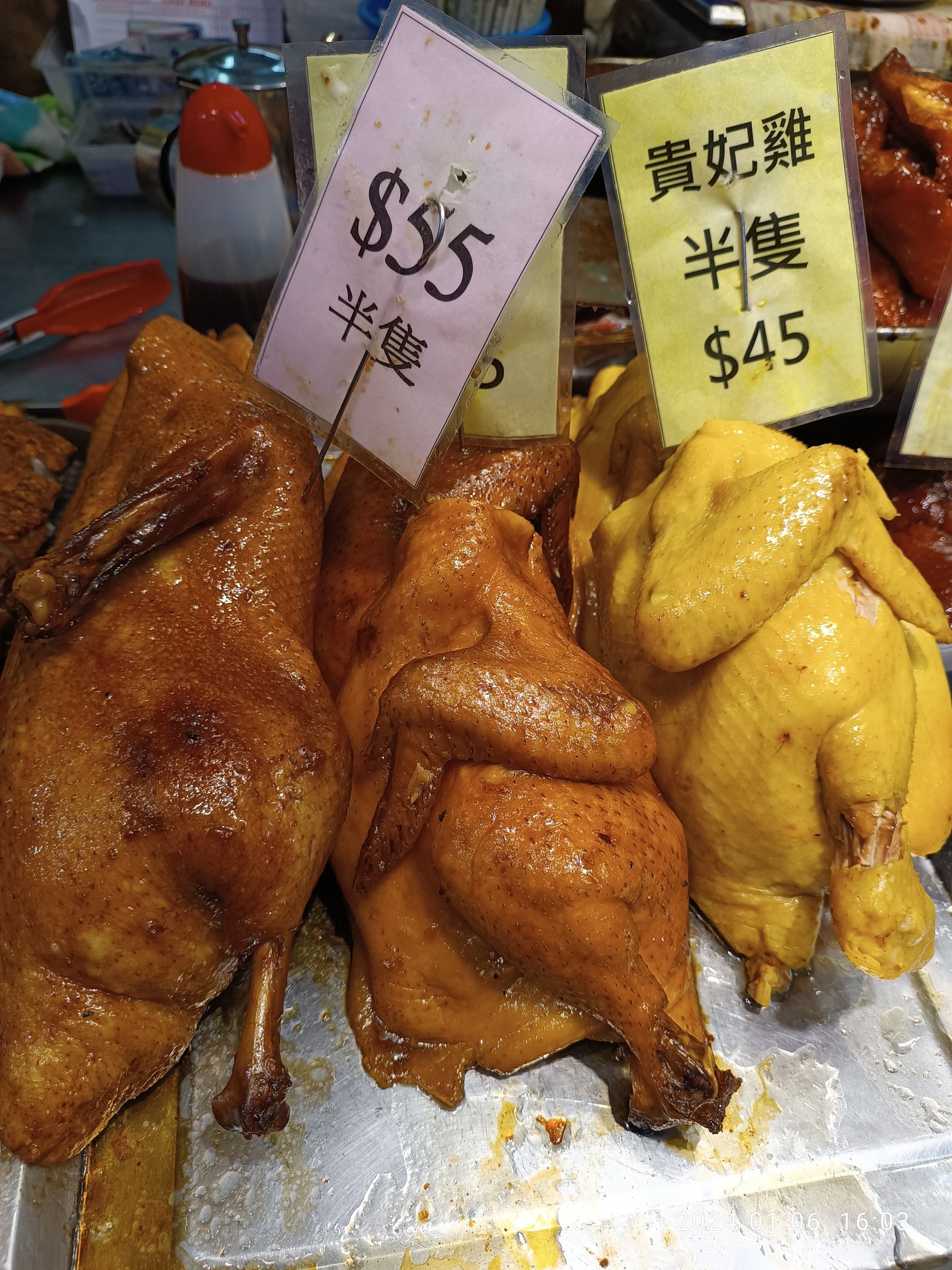 Eine Gruppe von Hühner auf einem Metalltablett mit Preisschildern in einem belebten Markt.