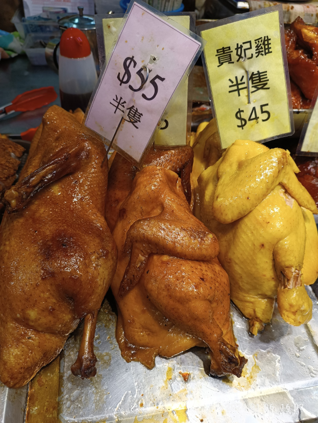 Eine Gruppe von Hühner auf einem Metalltablett mit Preisschildern in einem belebten Markt.