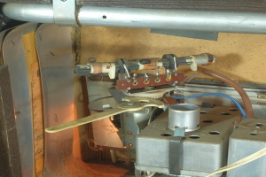 Ein Nahaufnahme eines Gasofens mit einem daran angeschlossenen Schlauch, umgeben von Metallobjekten, Rohren und verstreuten Werkzeugen und Materialien, was darauf hinweist, dass es repariert wird.