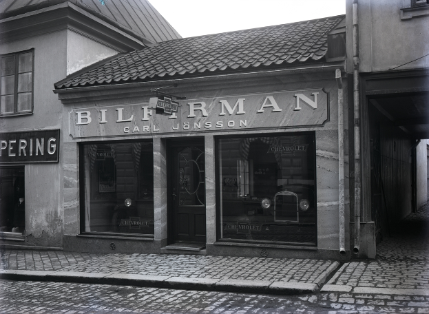 Ein Schwarz-Weiß-Foto eines Gebäudes mit einer Tafel, die 'Bilferman' lautet, mit Fenstern, einer Tür und Tafeln mit Text, sowie einer Straße unten.