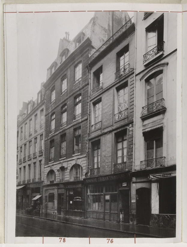 Schwarz-weißes Foto einer Stra├če mit Geb├Ąuden, Fenstern, Gel├Ąndern, Namensschildern und einer Stra├če unten.