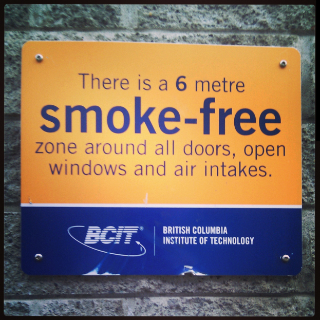 Ein Schild an einer Wand mit der Aufschrift '6 Meter rauchfreie Zone rund um Türen, offene Fenster und Luftansaugöffnungen'.