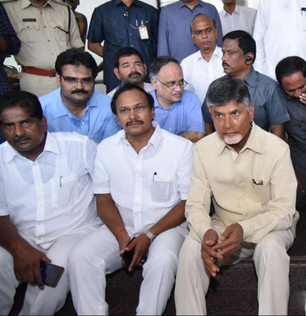 Andhra Pradesh Chief Minister Chandrababu Naidu und seine Kabinettsmitglieder sind zu einer Besprechung in Hyderabad versammelt, wobei einige Teilnehmer auf Treppen sitzen und mobile Telefone halten und andere im Hintergrund stehen.