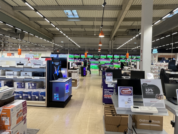 Großer Raum in einem Walmart-Laden voller Elektronik, die in Regalen angeordnet ist, einschließlich Computer und Drucker, mit Menschen auf dem Boden, einer Säule, Schildern, Deckenlampen und Deckenventilatoren.