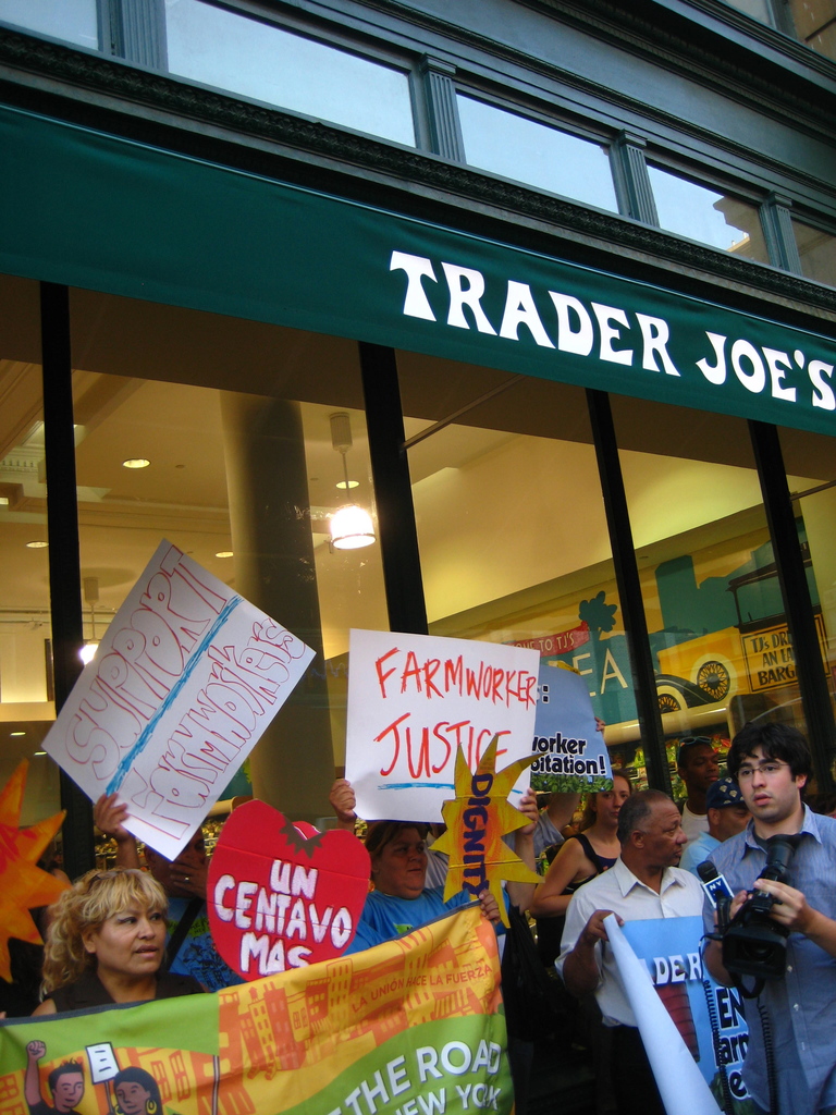 Eine Gruppe von Menschen, die vor einem Geschäft stehen und Schilder und Plakate halten, mit einer Säule und Lampen auf dem Dach im Hintergrund
