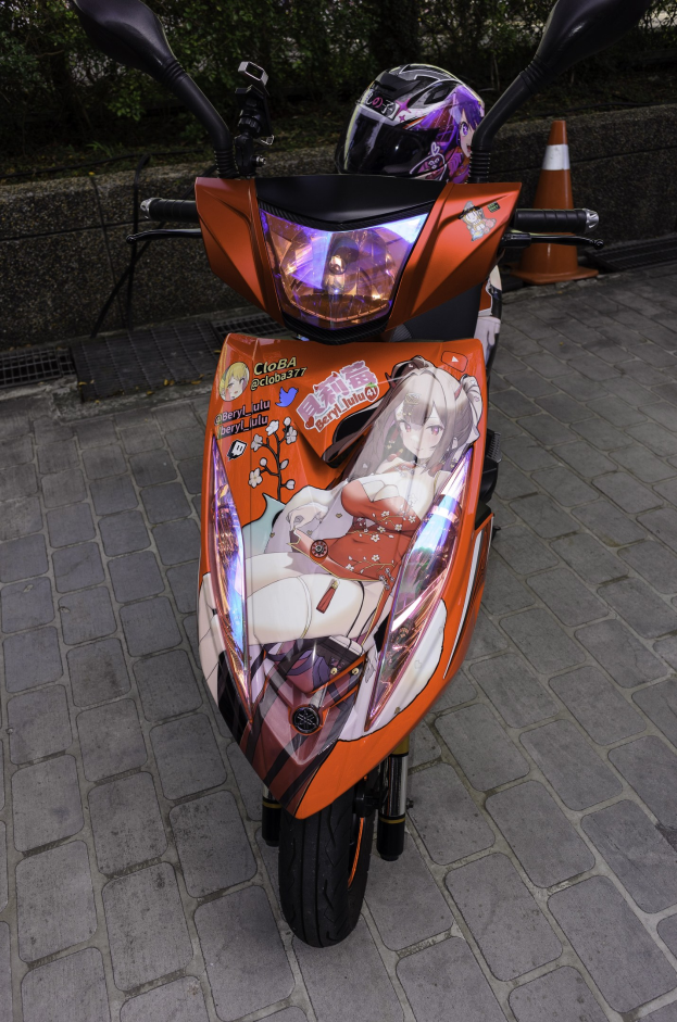 Ein oranger Roller auf einer Stra├če mit einem Helm daneben, neben einem Verkehrskegel, einer Wand und B"umen im Hintergrund.