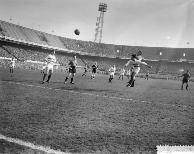 Eine Gruppe von Männern, die auf einem Feld mit Stadion, Flutlicht und klarem Himmel Fußball spielen.
